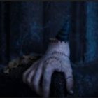 Pale hands with dark veins and blood spots adorned with silver rings on a dark backdrop.