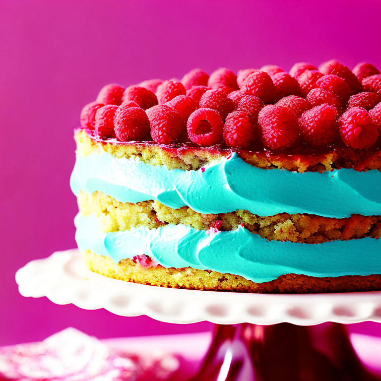 Colorful Layered Cake with Turquoise Frosting and Raspberries on Pink Background