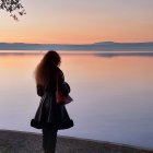 Woman admiring serene sunset over water with pagoda and mountains in distance