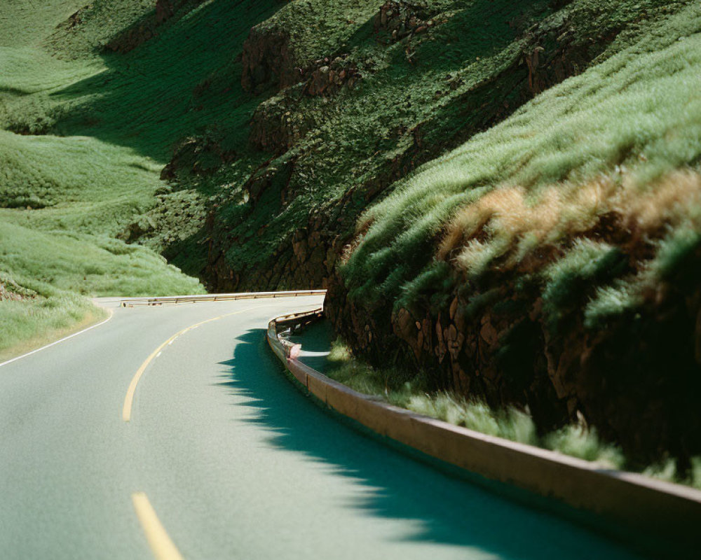 Scenic curvy road through lush green hills and sharp cliffs under a bright sky