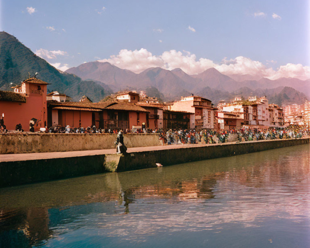 Riverfront with Terracotta-Roofed Buildings and Mountains in Background