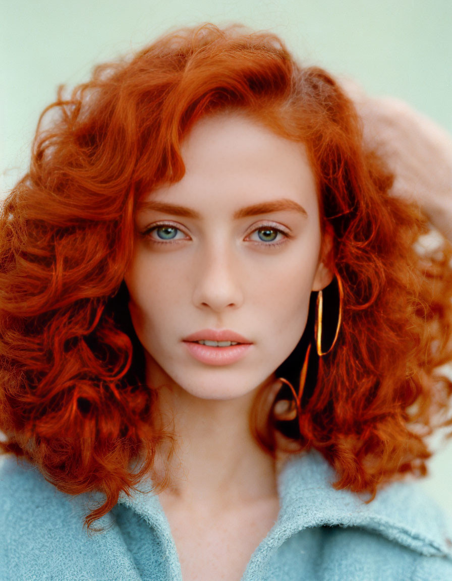 Vibrant red curly hair woman with blue eyes and gold earrings in turquoise coat