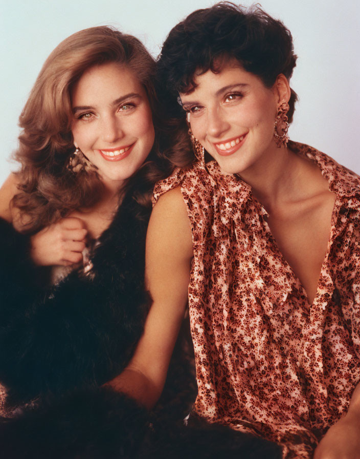 Two women posing closely, one blond in fur, the other with dark curly hair in leopard print top
