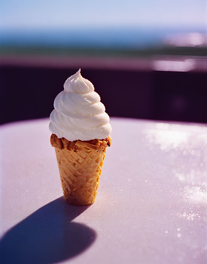 Vanilla soft serve ice cream cone shadow on table with blue sky and ocean background