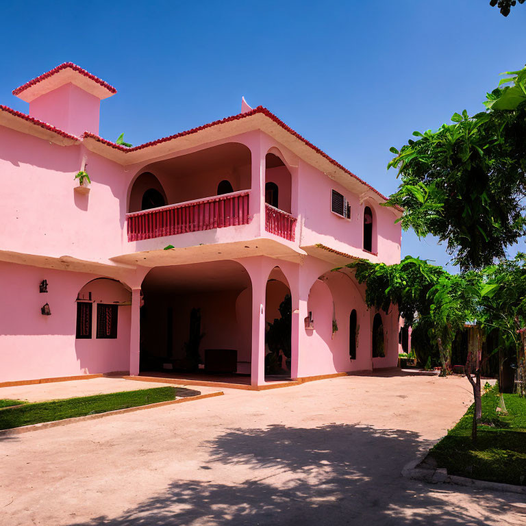 Pink Two-Story Building with Balconies and Arched Doorways in Greenery under Blue Sky