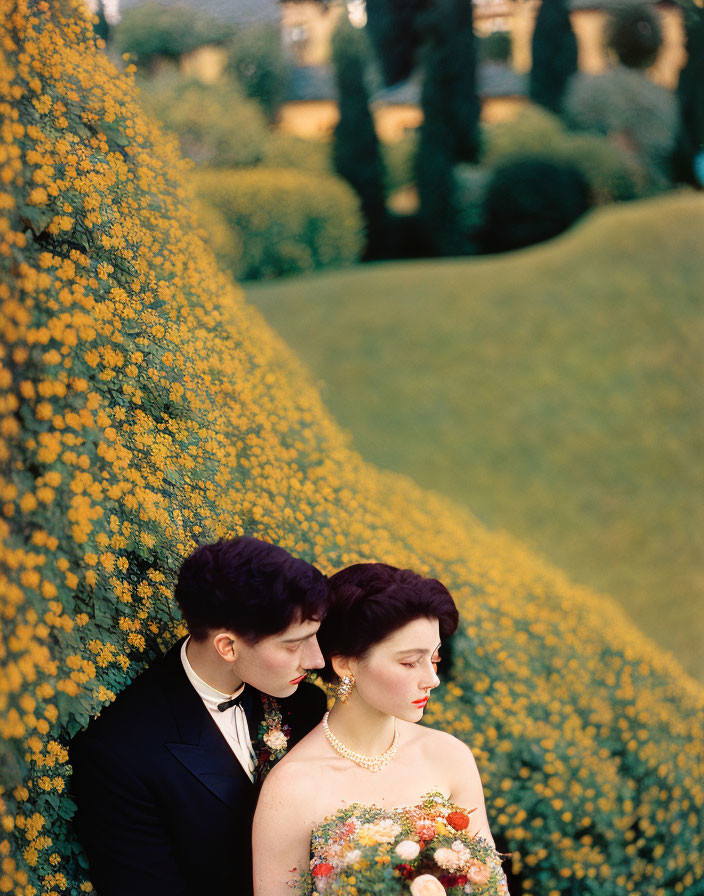 Formal couple embraced in front of vibrant yellow flowers and greenery