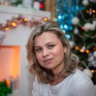 Blond woman sitting by Christmas tree with white and gold ornaments