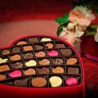 Heart-shaped box with assorted chocolates and white roses on red background