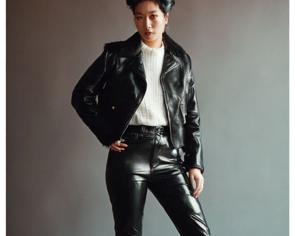Fashionable person in black leather jacket and pants with white sweater posing confidently.