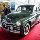 Classic Green Car Displayed at Indoor Car Show with Red Carpet and Classic Cars in Background