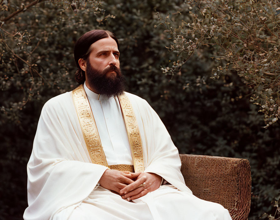 Bearded Man in White Robe with Golden Embroidery Contemplates Chair in Greenery
