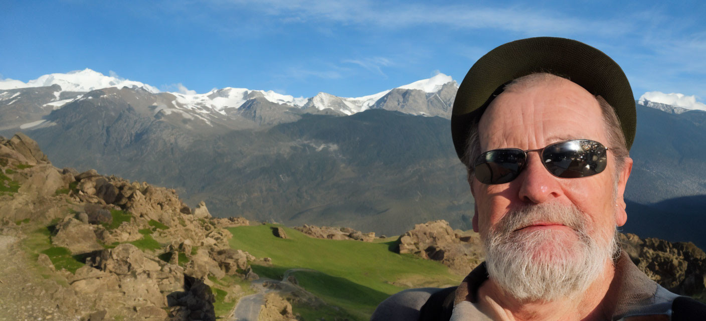 Bearded man in sunglasses takes selfie with mountains and valley backdrop