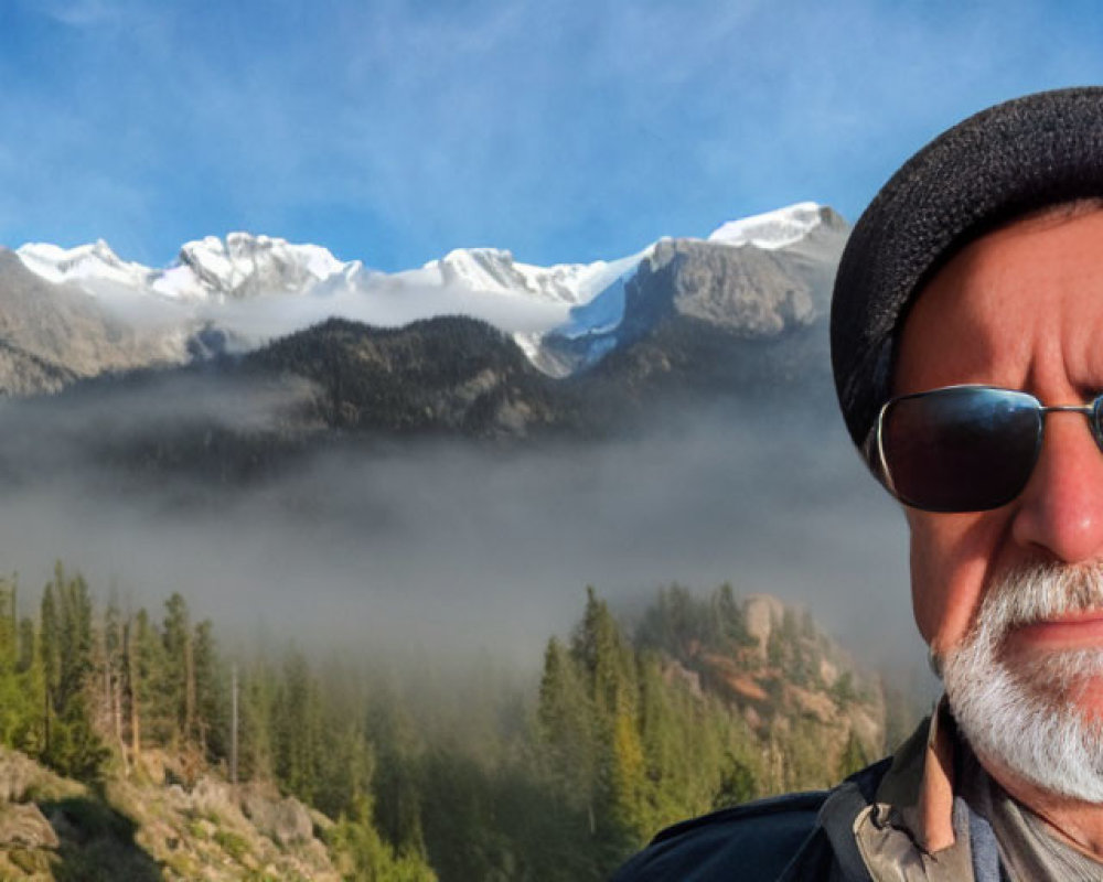 Man in Sunglasses and Hat Posing in Front of Misty Snow-Capped Mountains
