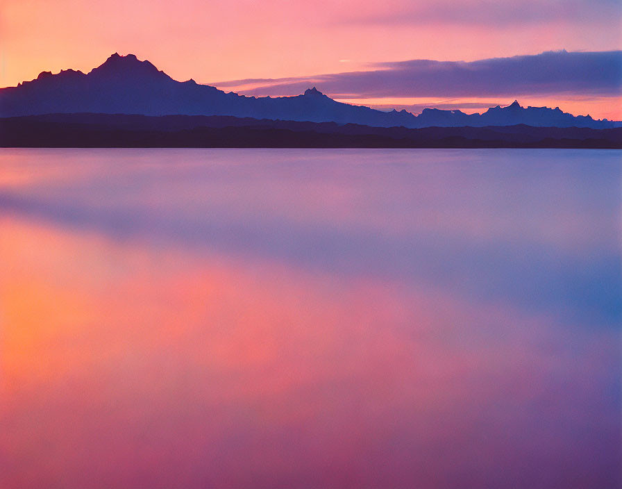 Tranquil lake at sunset with silhouetted mountains and gradient sky