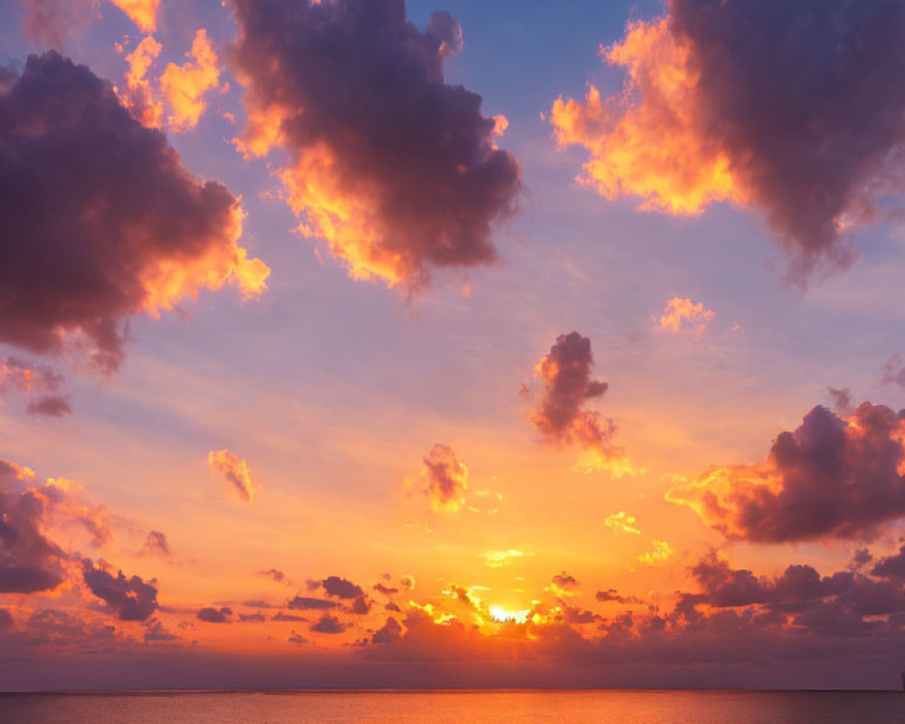 Colorful sunset over ocean with sun and clouds casting warm hues.