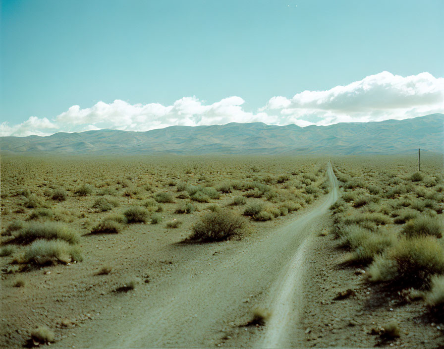 Desert Landscape with Dirt Road and Rolling Hills Under Blue Sky