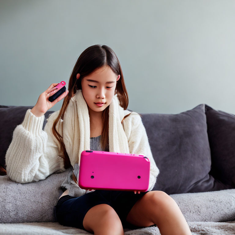 Young girl on sofa with pink tablet brushing hair