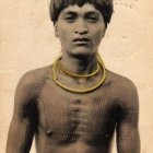 Young man with tribal tattoos and necklace against warm backdrop