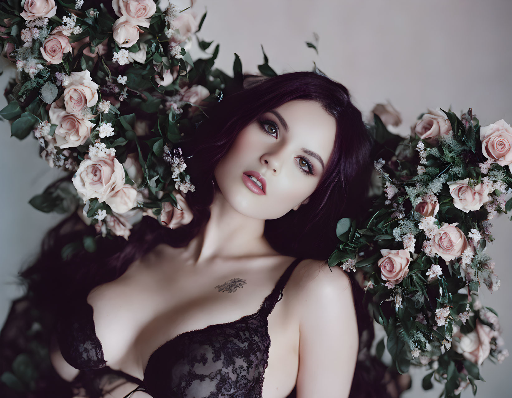 Dark-haired woman in black lace under floral arch gazes at camera