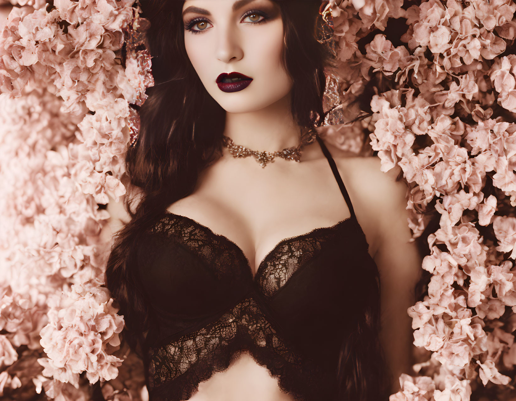 Dark-haired woman in lace garment amid pink blossoms with choker necklace