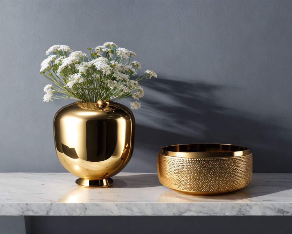 Golden vase and bowl with white flowers on marble countertop against grey wall