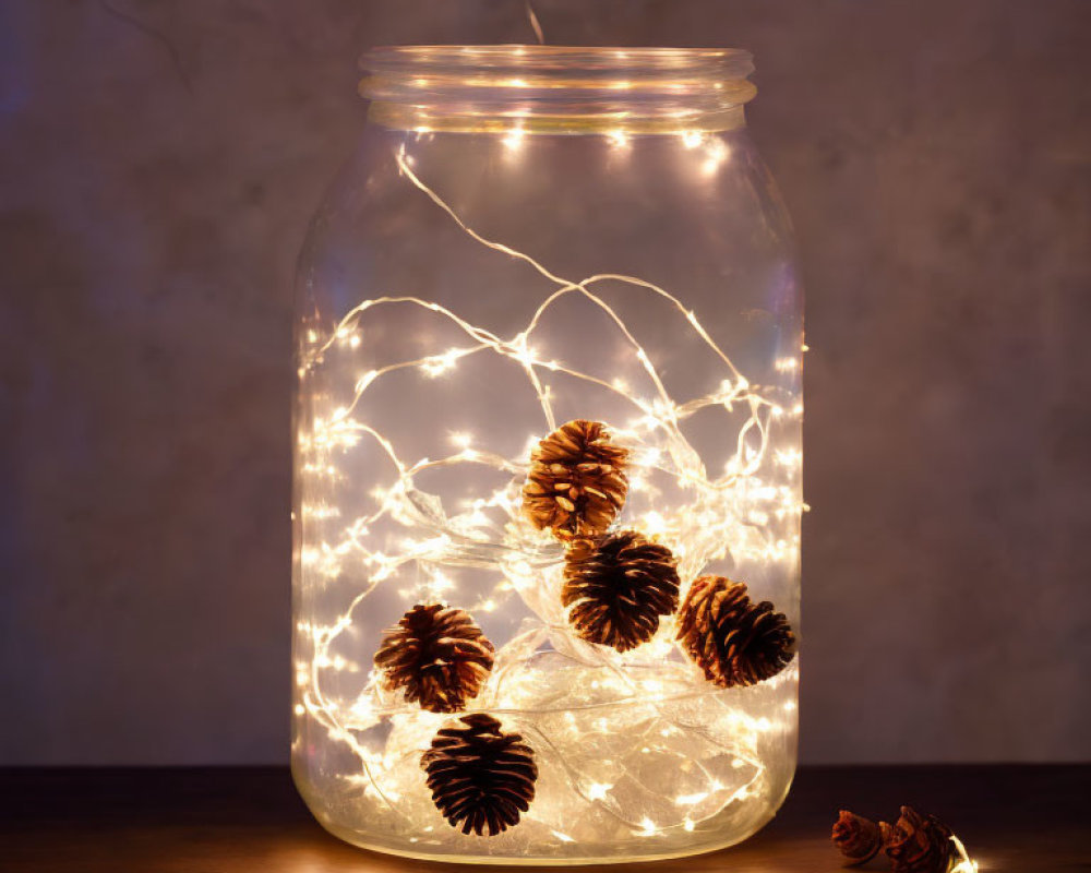 Glass jar with string lights and pine cones on wooden background