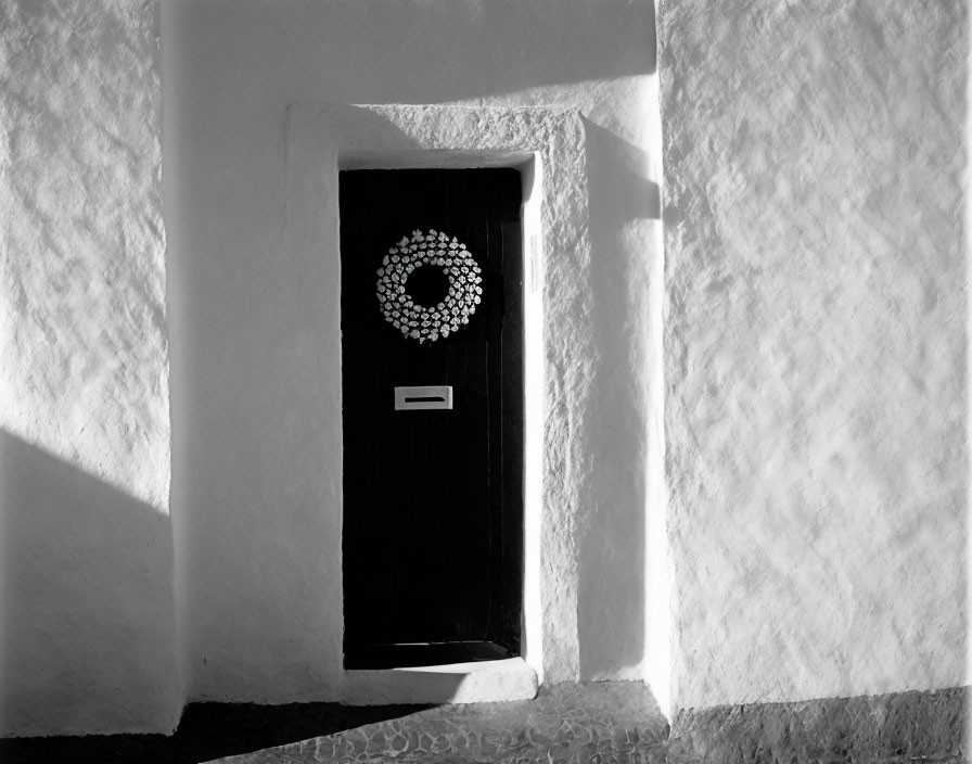 Monochromatic palette: Black door, wreath, white wall, strong shadow