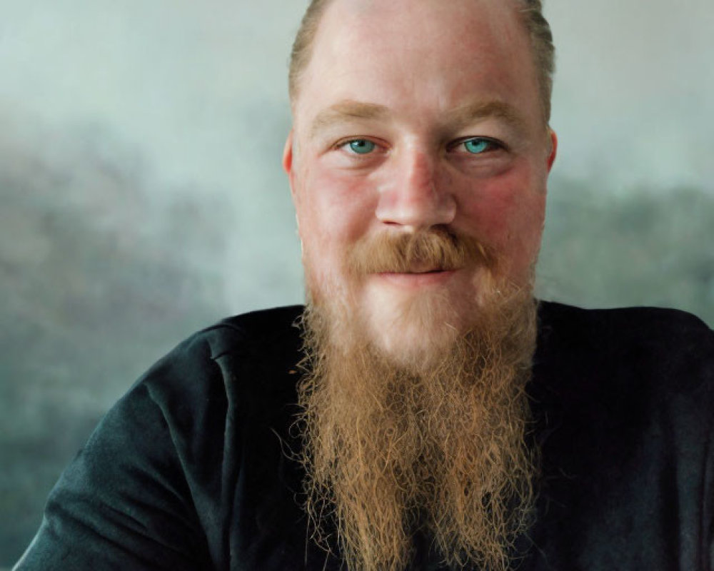 Smiling person with long beard, mustache, blue eyes, and tattoo on arm