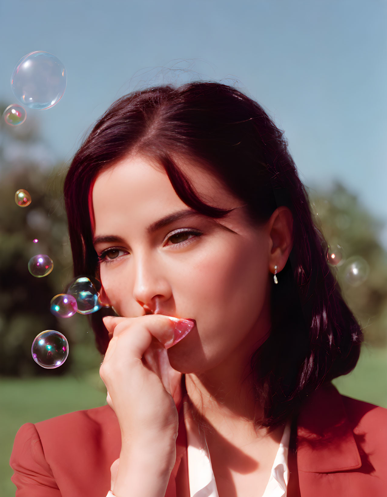 Woman in Red Jacket with Finger on Lips Surrounded by Bubbles in Green Outdoor Setting