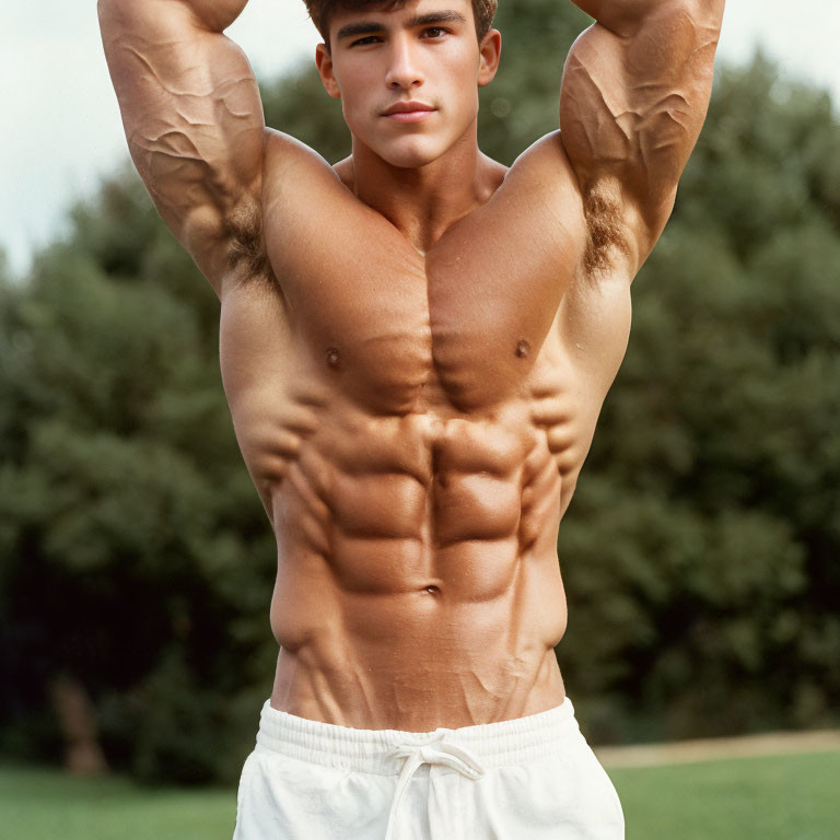 Muscular male with six-pack and arms stretching in white pants outdoors