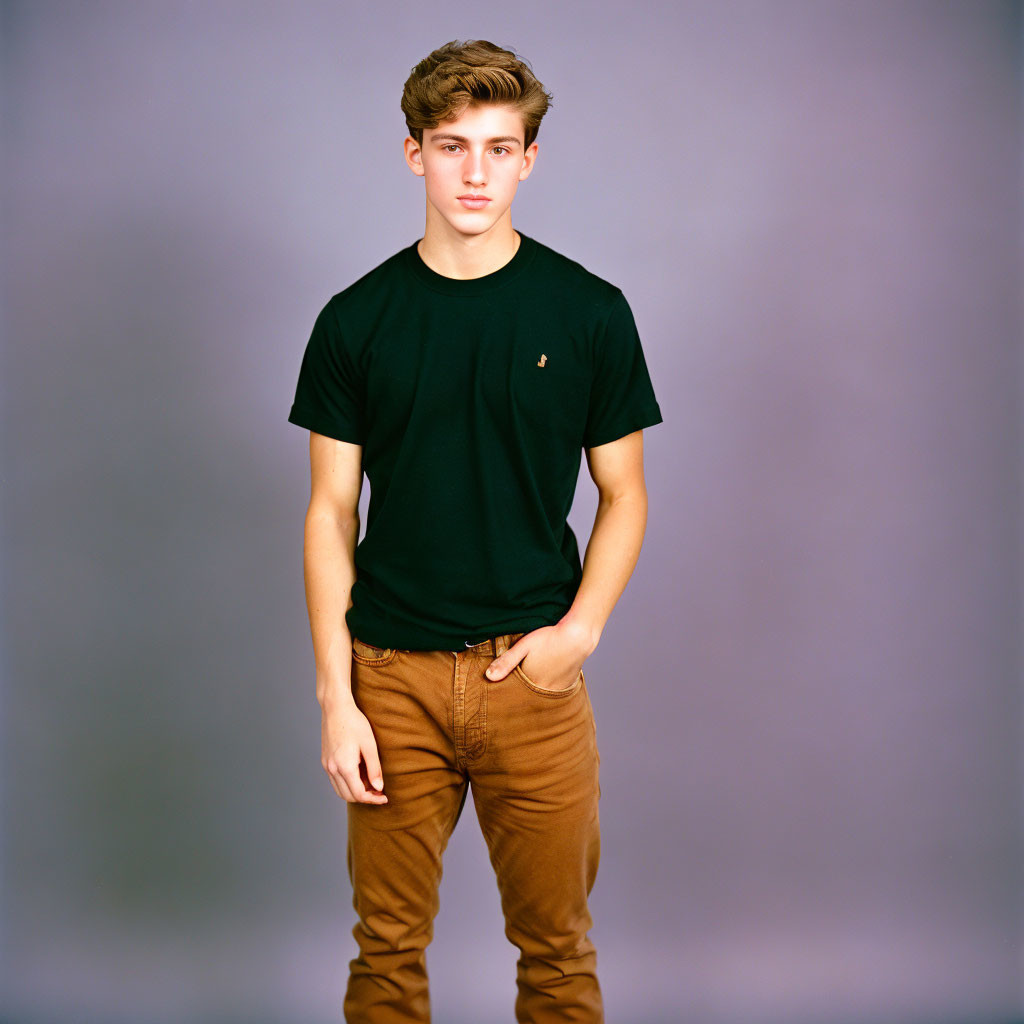 Young man in black t-shirt and brown trousers against gray background