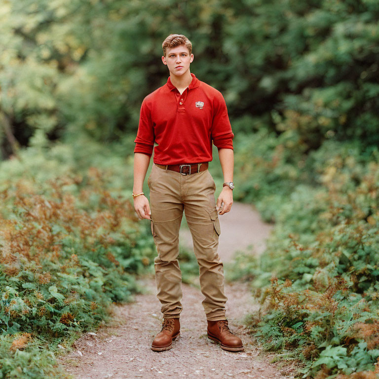 Young man in red polo shirt and khaki pants on forest trail gazes at camera