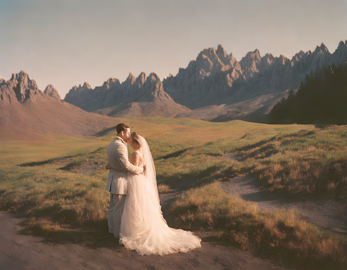 Bride and groom embrace in serene meadow with dramatic mountain peaks.