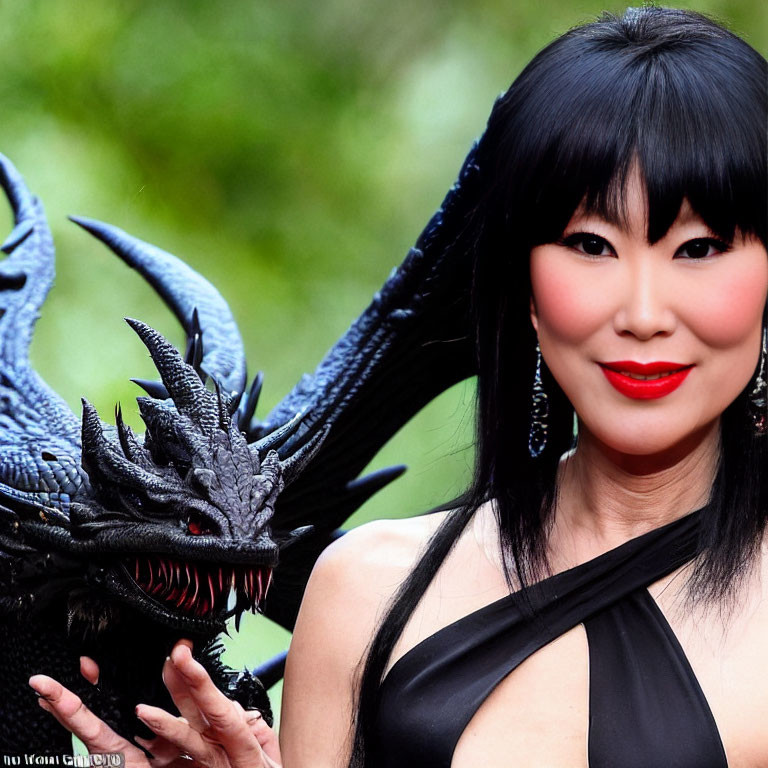 Black-haired woman with red lipstick holding dragon prop, smiling against green background