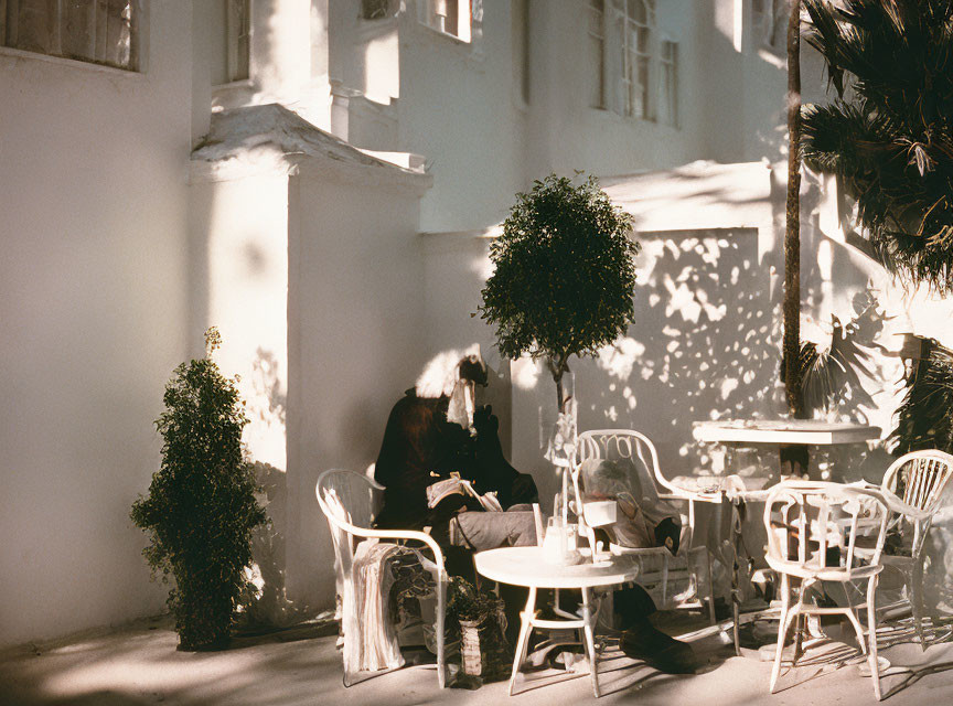 Person at Cafe Table in Shadow-Patterned Courtyard