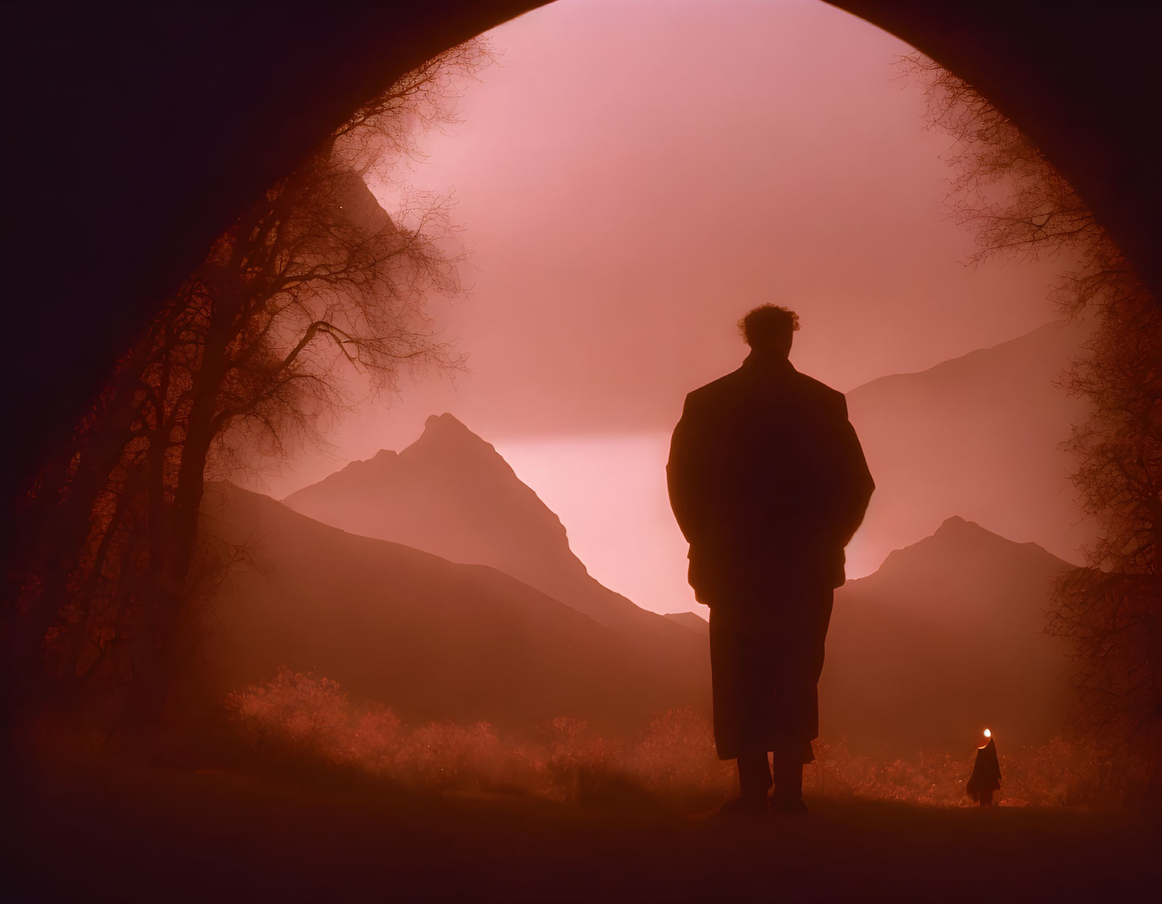 Silhouetted Figure in Cave Entrance Overlooking Mountains at Dusk