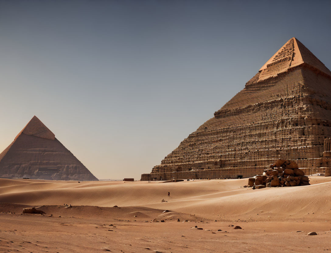 Ancient Egyptian pyramids under clear sky with person walking in desert.