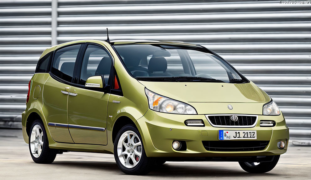 Metallic Olive Green Hatchback Car with Alloy Wheels Parked in Front of Corrugated Metal Background