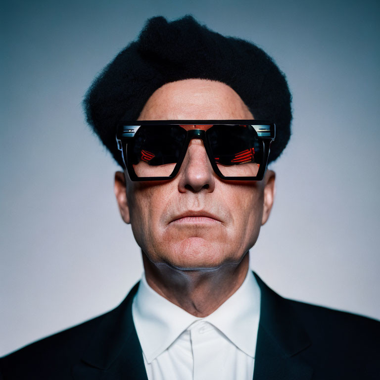 Stoic man in futuristic sunglasses and black suit with voluminous hair on grey background