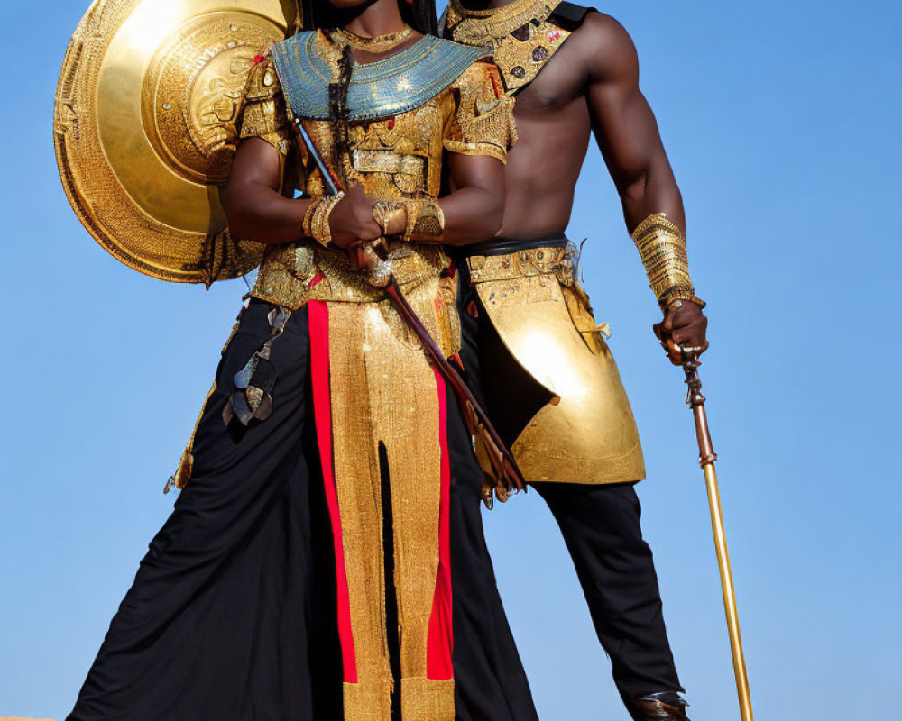 Two individuals in golden and black warrior attire with shield and spear under clear blue sky.