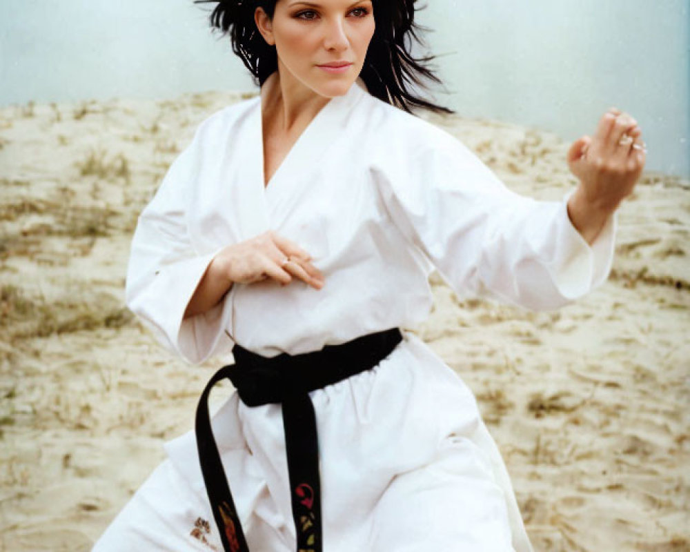 Person in white karate gi and black belt striking a pose on sandy beach with calm lake and over