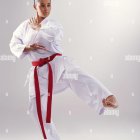 Karate practitioner in red and black belt performing high kick pose.