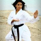 Person in white karate gi and black belt striking a pose on sandy beach with calm lake and over