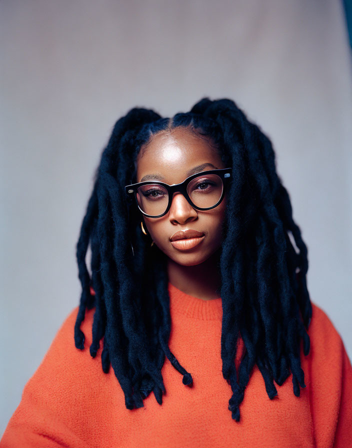 Woman with Thick Braids and Glasses in Orange Sweater on Blue Background
