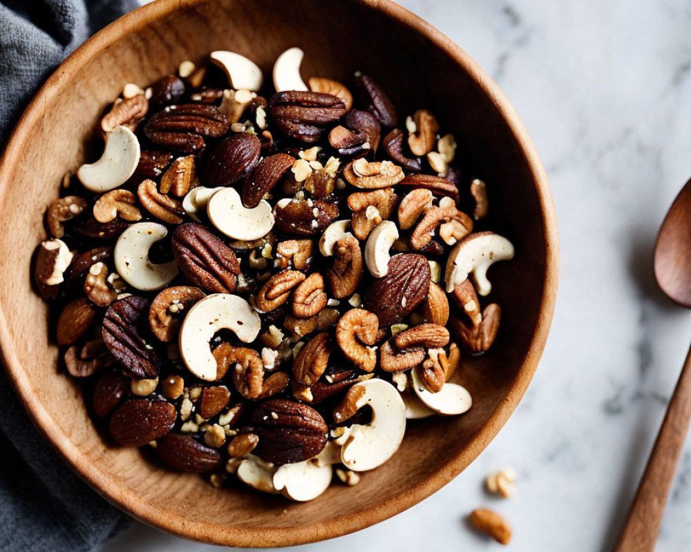 Wooden bowl with almonds, cashews, and pecans on marble surface.