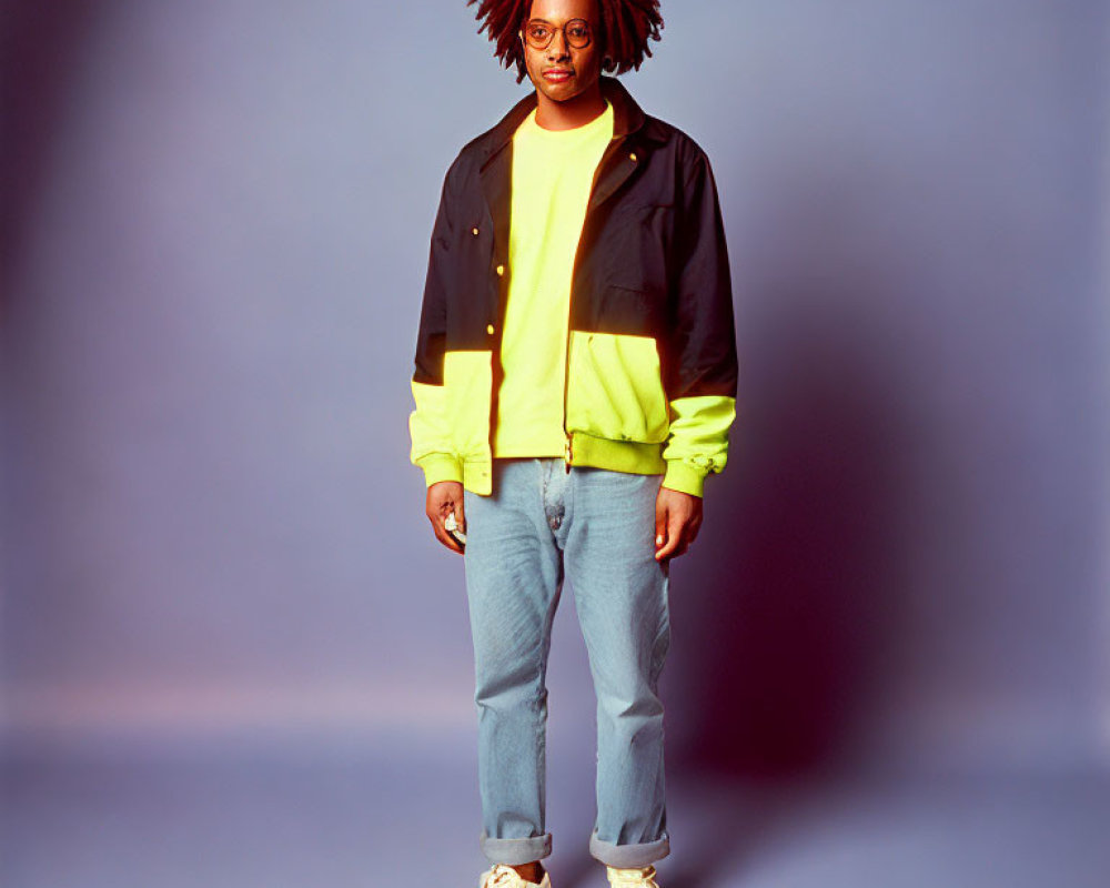Person with dreadlocks in black and neon jacket, blue jeans, white sneakers on blue background