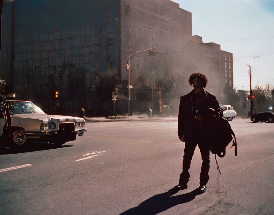 Urban scene: Person with afro crossing street in sunlight.
