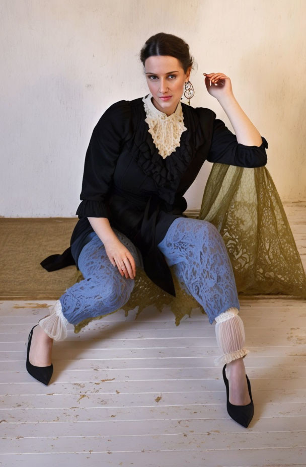 Woman in black blouse and lace trousers sitting against draped gold fabric object