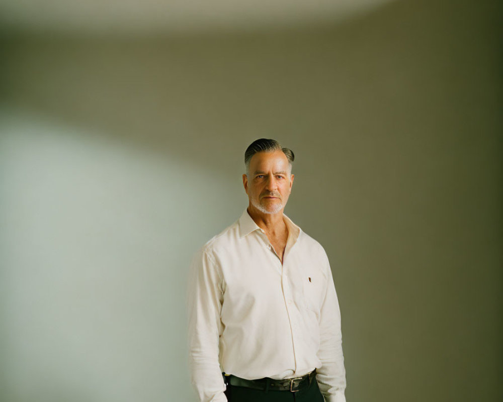 Confident man in white shirt and dark pants against neutral backdrop