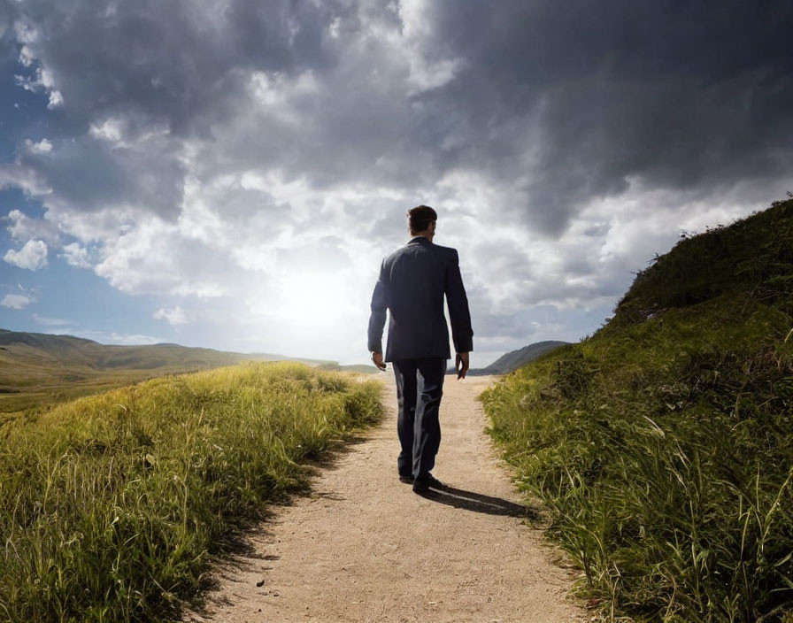 Businessman walking on grassy path under dramatic sky